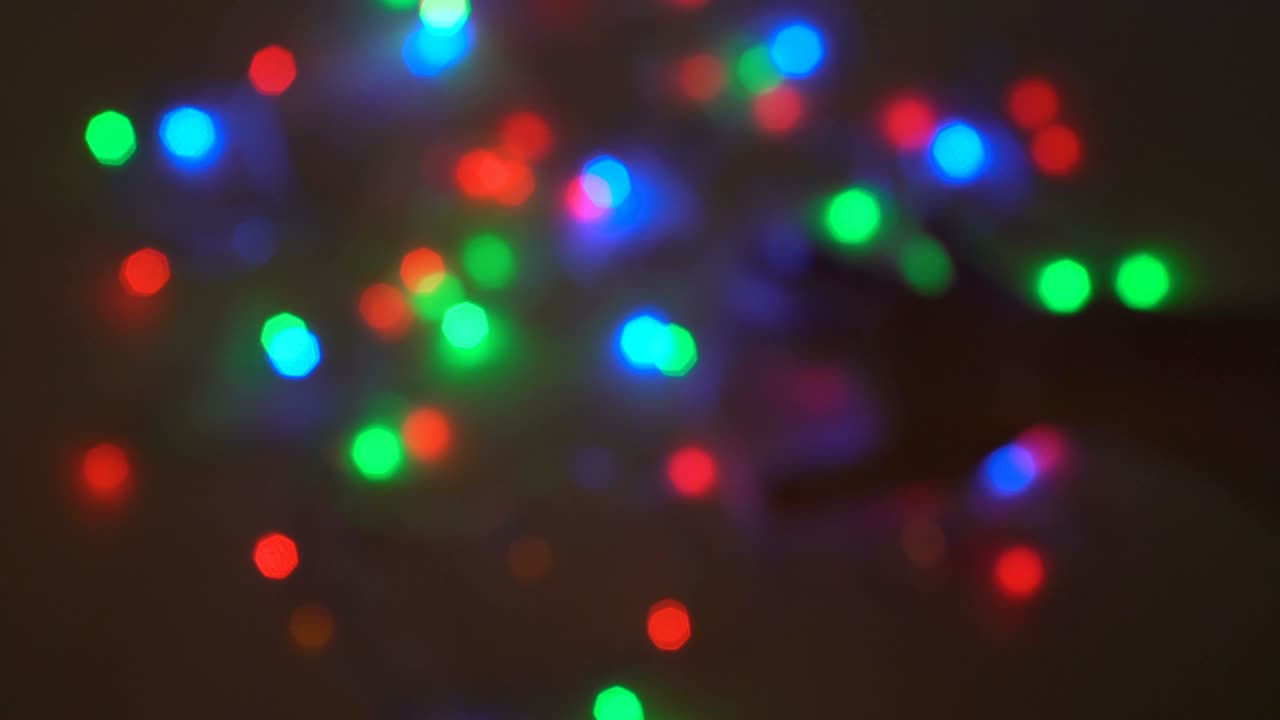 luces navideñas inusuales. primer plano, manos masculinas borrosas mezclando luces intermitentes multicolores en un fondo negro. silueta. fondo borroso. 4k.