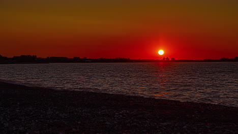 Eine-Zeitrafferaufnahme-Eines-Sonnenaufgangs-An-Einem-Flussufer-Mit-Einem-Felsbett-In-Der-Nähe-Einer-Landschaft