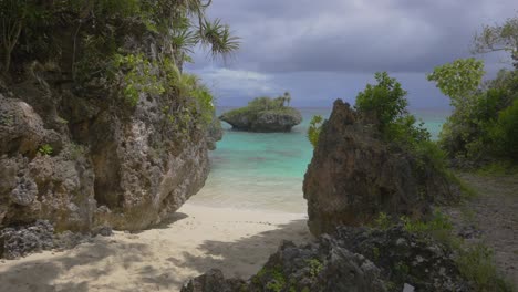 Eine-Kleine-Felsige-Insel-Vor-Einem-Tropischen-Strand,-Die-Das-üppige-Grün-Und-Die-Sandige-Küste-Kontrastiert-Und-Einen-Malerischen-Blick-Auf-Das-Idyllische-Tropische-Paradies-Bietet