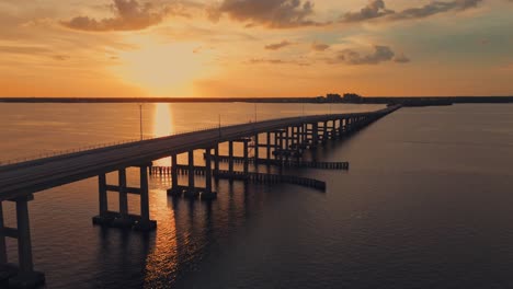 aerial wide shot of caloosahatchee bridge leading to north fort myers city in background. golden sunset time in florida. orange colored sky. silhouette of construction