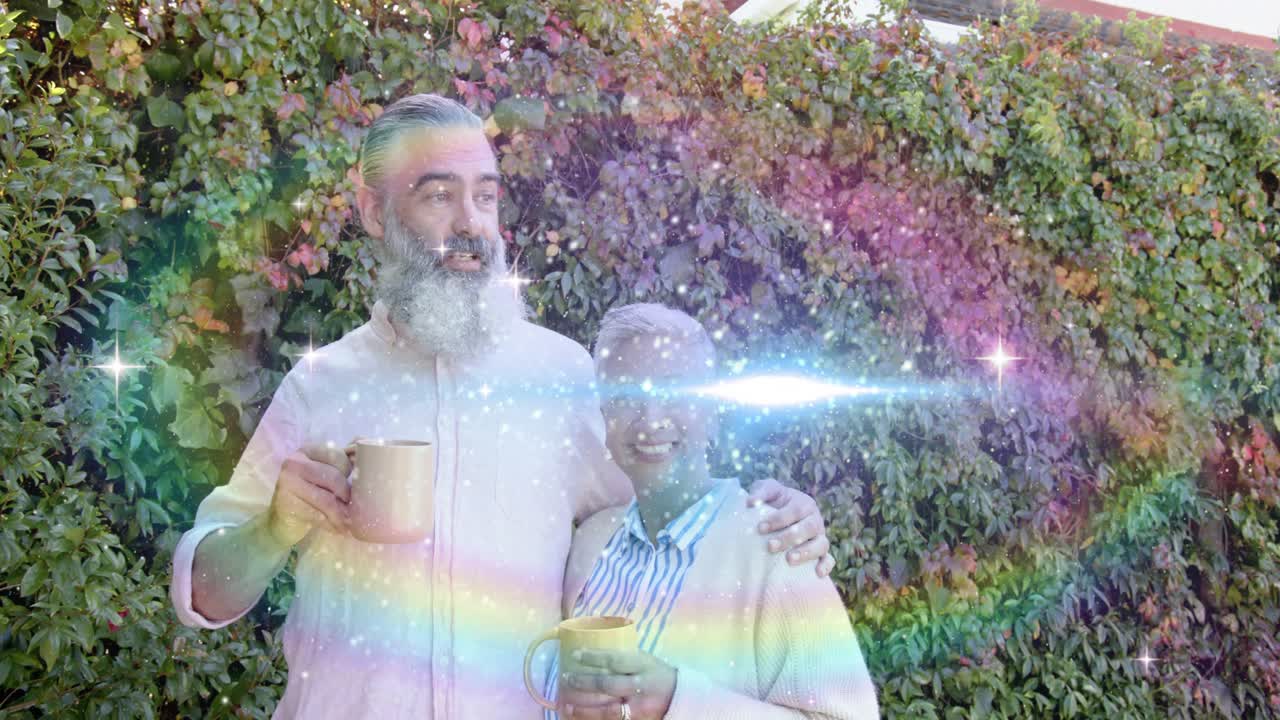 Man and woman holding mugs by hedge, sparkling rainbow appearing from left across faces, marketing