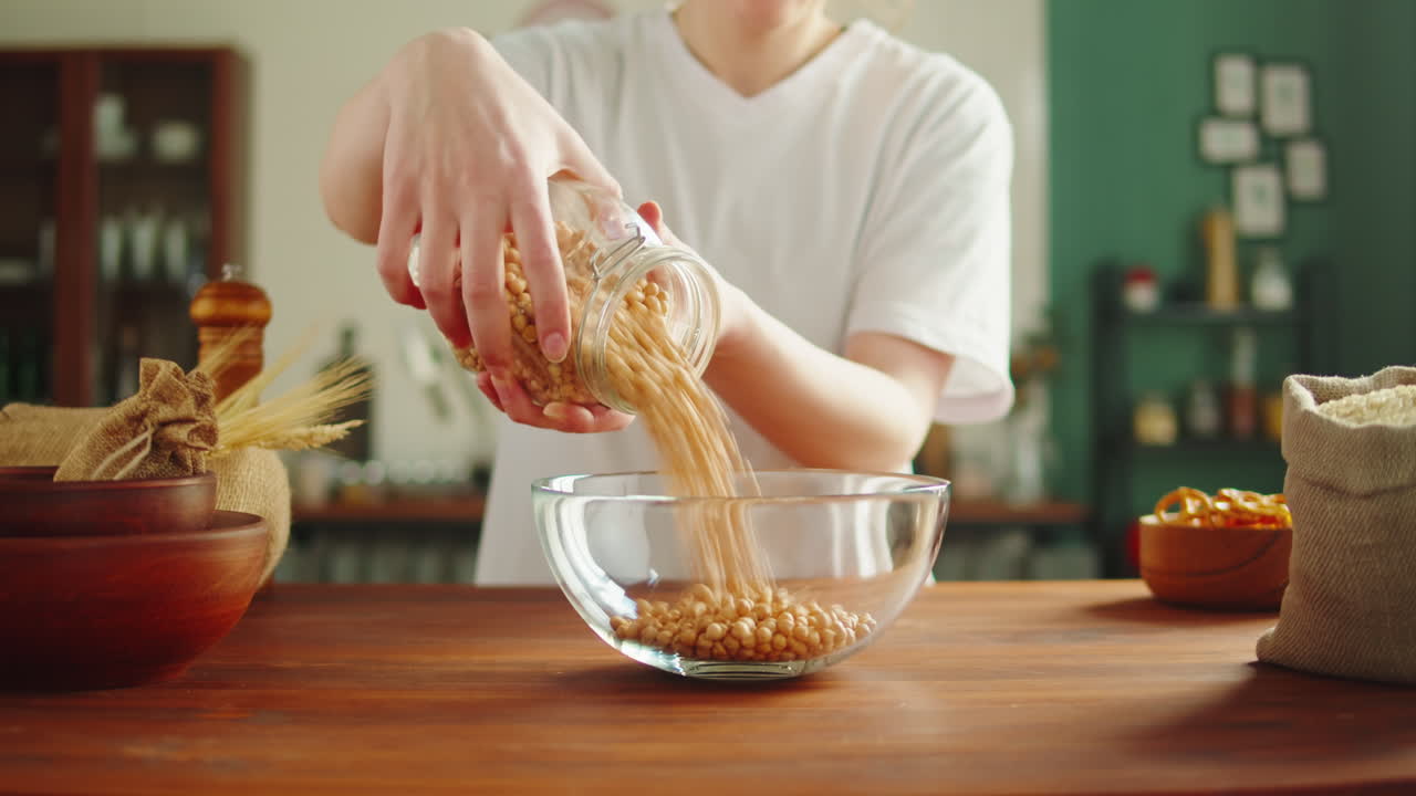 Person pouring chickpeas from a jar into a bowl in a kitchen
