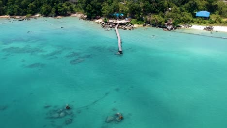 Aerial-of-beautiful-turquoise-blue-sea-with-old-wooden-pier-Koh-Rong-Sanloem,-Cambodia