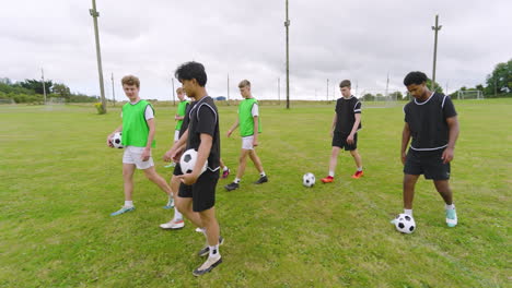 multiracial male soccer players leaving pitch and walking with footballs