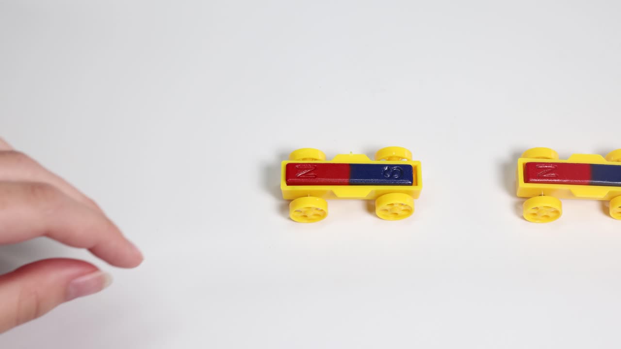 Hands manipulate magnetic toy cars on a white surface, illustrating magnetic attraction and repulsion in a well-lit environment