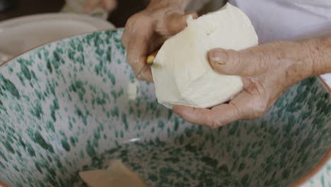 a woman in italy cutting up a ball of mozzarella into a bowl full of water