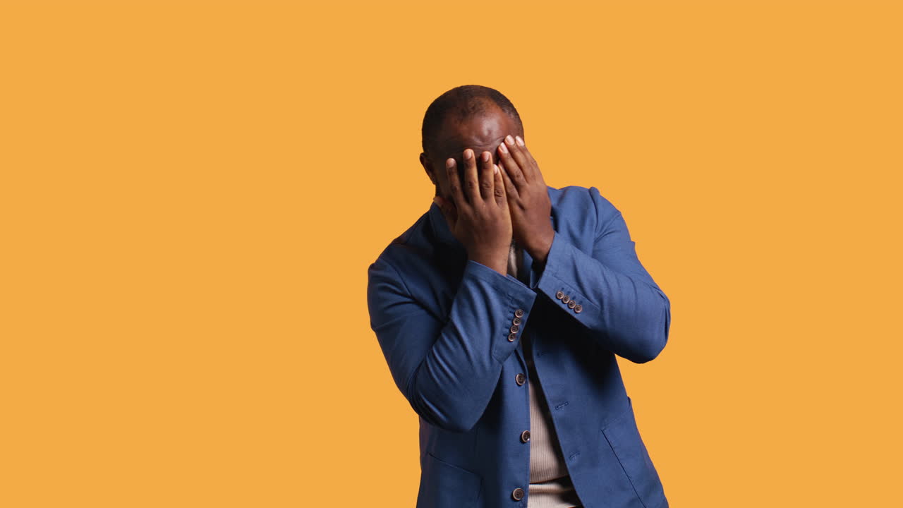 Man covering face with hands to avoid being recognized, studio background