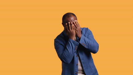 man covering face with hands to avoid being recognized, studio background