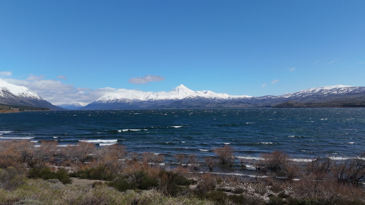 Turquoise waves of Huechulafquen lake breaking on shore with Lanin volcano in background. Patagonia, Neuquén, Argentina
