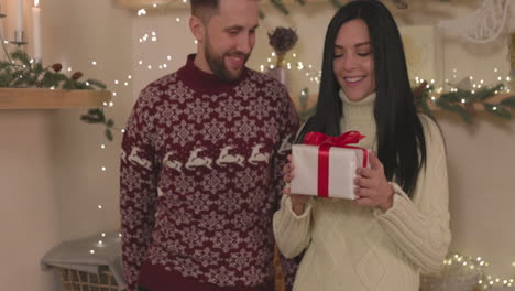Happy-Woman-Shaking-A-Christmas-Gift-Box-With-Her-Boyfriend-At-Home