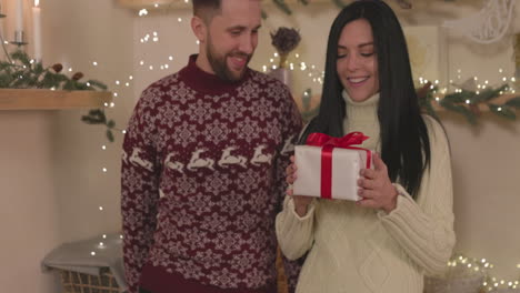 mujer feliz sacudiendo una caja de regalo de navidad con su novio en casa