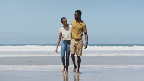 happy african american couple hugging each other and walking at the beach