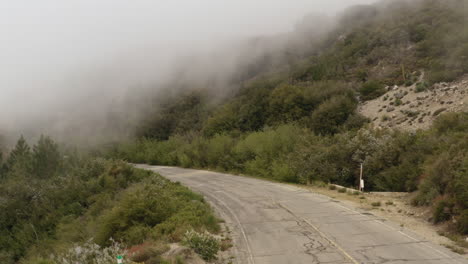 drone flying over an asphalt mountain road surrounded by green bushes