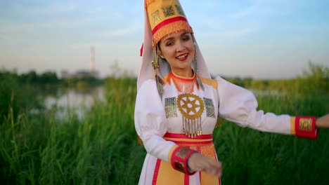 attractive young woman in folk mari people costume is dancing outdoors