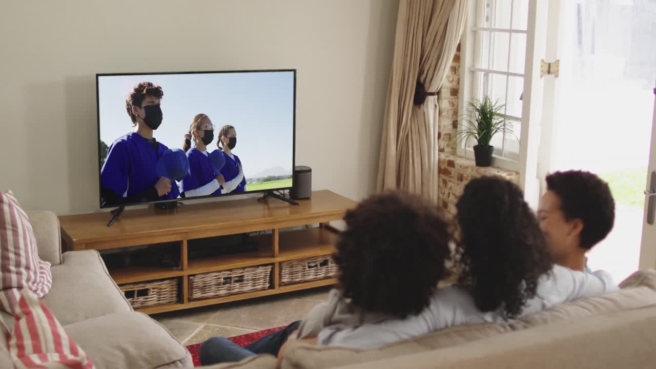 Famiglia felice seduta a casa insieme che guarda una partita di baseball in TV durante il COVID-19
