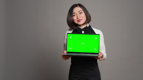 asian server presenting greenscreen display on laptop in studio