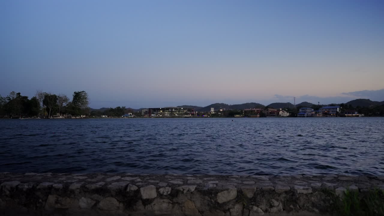 Peaceful Lake Peten Itza from Flores with calm water and distant mountains, low static establishing at dusk evening
