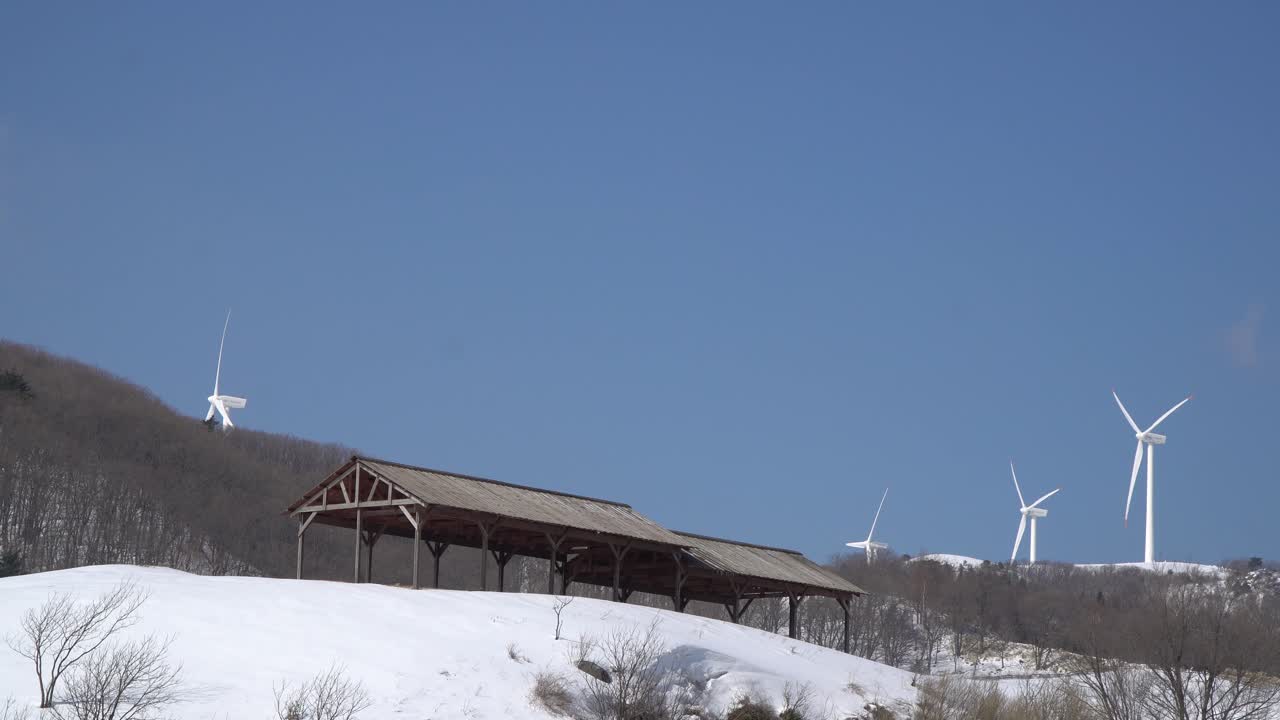 풍력 터빈 프로펠러가 한국의 눈 덮인 산에서 움직이고 하늘을 만지고 있습니다.