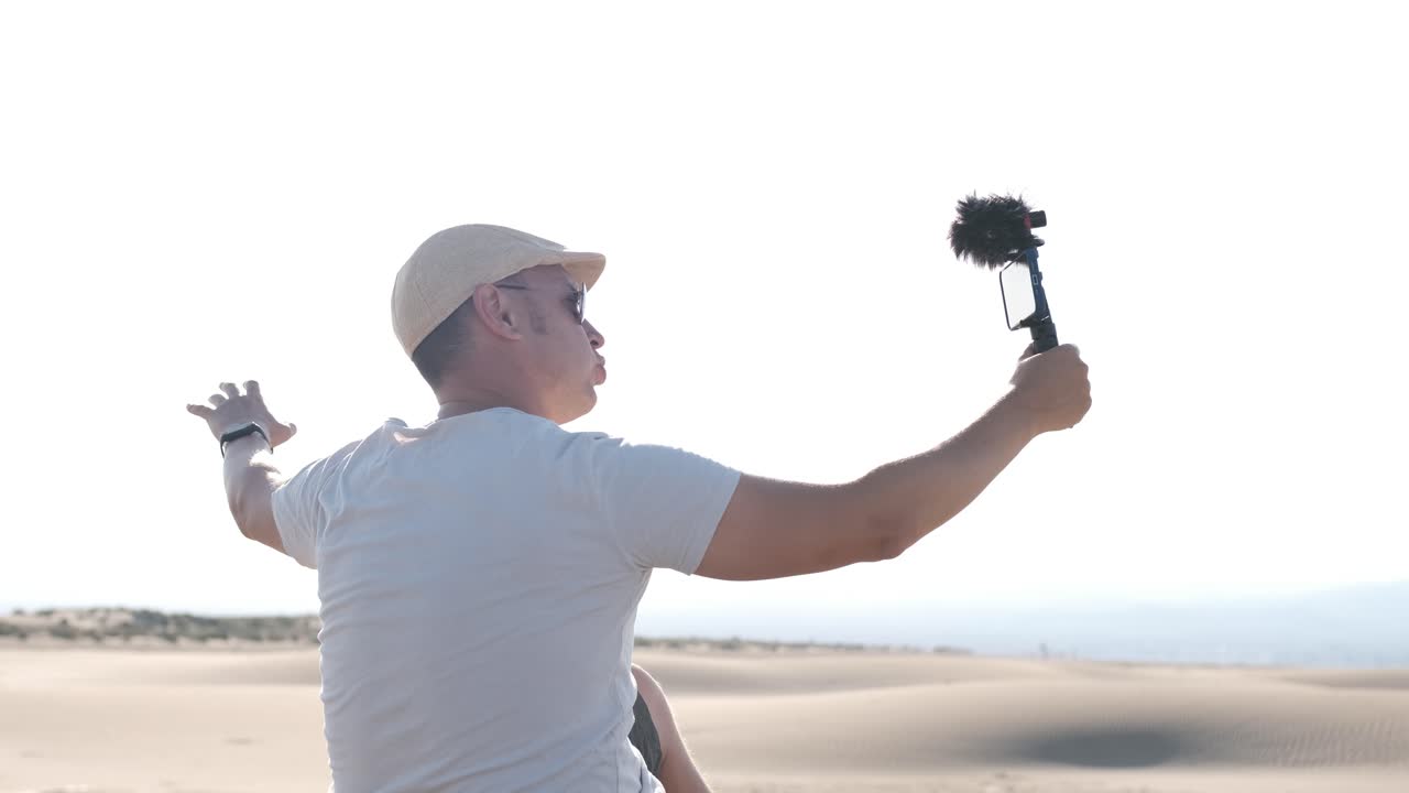 Man filming himself with his cell phone in the desert dunes. Traveling male content creator