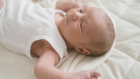 close up view of a baby in white bodysuit lying on bed moving his arms