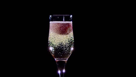 mellow Strawberry in Glass with Champagne Sparkling Wine Slow Motion Mellow Strawberry in Glass with Champagne Sparkling Wine Alcohol Drink Lathers and Bubbles Appear Tall Glass Shines in Different Colors Fruit Red Color Slow Motion side View Black Background Studio