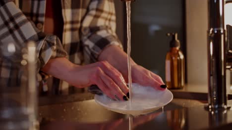 Close-up-a-brunette-girl-in-a-checkered-shirt-and-black-manicure-washes-the-dishes-while-her-brunette-boyfriend-in-a-gray-T-shirt-hugs-her-in-a-modern-kitchen-in-the-evening-in-a-modern-apartment