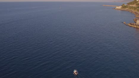 Aerial-view-of-boat-on-calm-sea-with-people-during-sunset,-Cefalu,-Sicily,-Italy