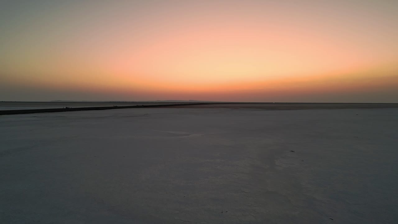 An aerial view of the Rann of Kutch, Gujarat, India reveals an endless white salt desert glowing under a vibrant sunset, casting warm hues across the vast 4K
