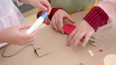 madre y hija bi-raciales felices pegando recortes coloridos en la sala de estar soleada