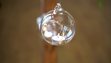 Single-small-candle-hanging-in-a-glass-lamp-inside-a-brick-building