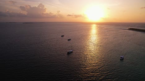 Magischer-Romantischer-Sonnenuntergang-Auf-Einer-Abgelegenen-Insel-Auf-Den-Malediven-Mit-Booten-Im-Vordergrund-Während-Der-Goldenen-Stunde,-Drohnenaufnahme-Mit-Wunderschöner-Reflexion