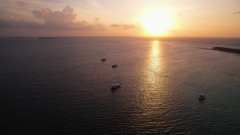 puesta de sol mágica y romántica en una isla remota en maldivas con barcos en primer plano durante la hora dorada, toma de drones con un hermoso reflejo