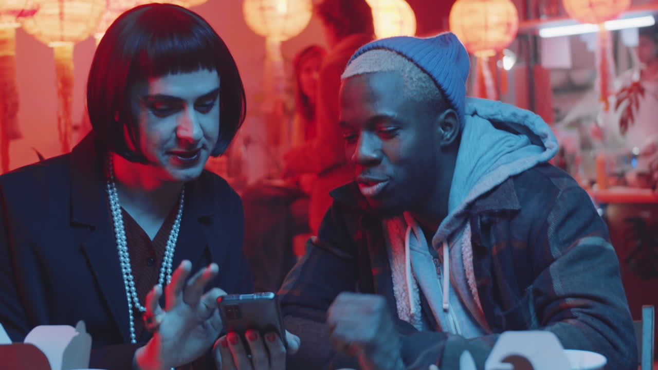 hombre transgénero usando un teléfono inteligente y hablando con un amigo negro