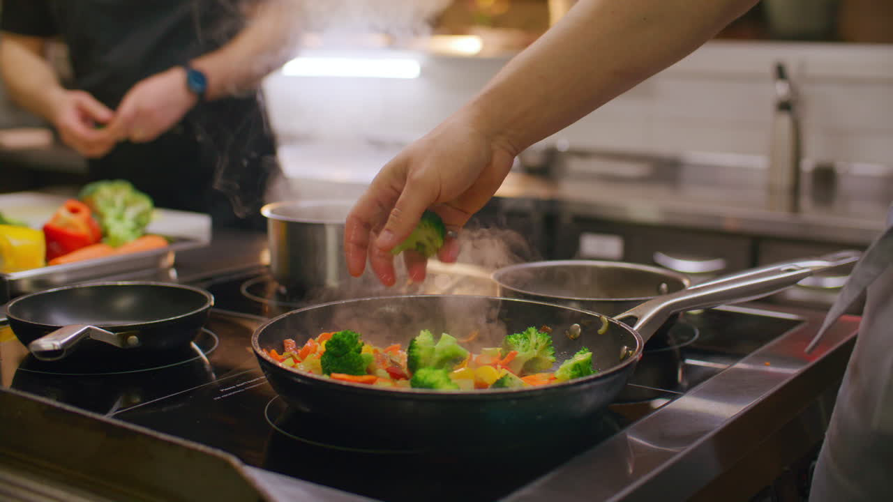 Kock lägger till färsk broccoli och vänder wokgrönsaker i stekpanna