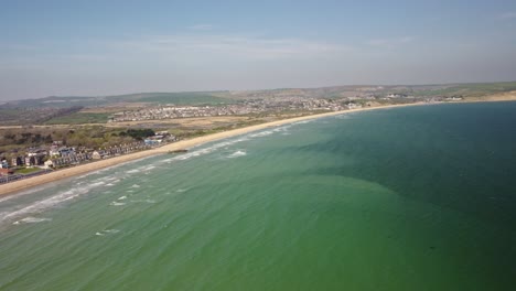 Drone video over the Weymouth Beach Bay Sea. The ocean, waves landing on the sand and surrounds town and fields. Sunny day wide view of the area. Shadow over the sea.