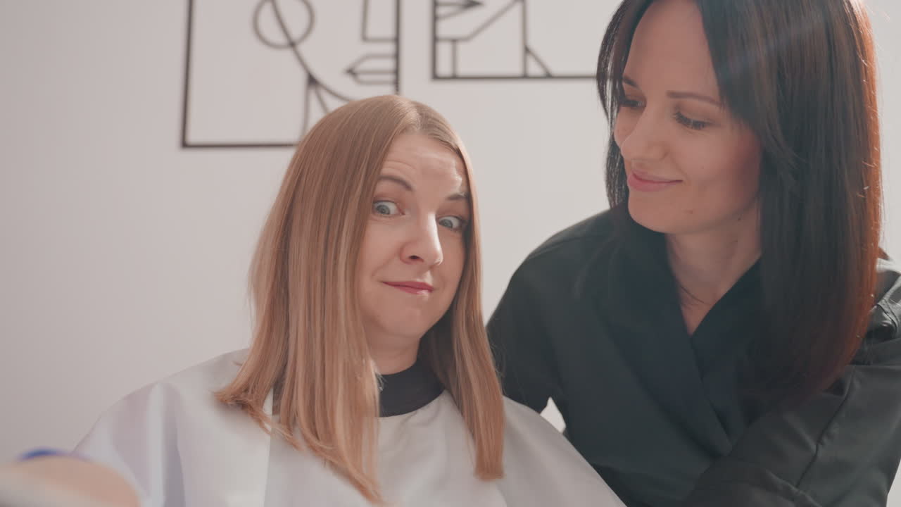 Estilista caucásico y cliente revisando la paleta de muestras de color, muestra rosa cerca del cabello trenzado, capa sobre el cliente, iluminación suave y brillante, expresiones alentadoras, interior de salón moderno