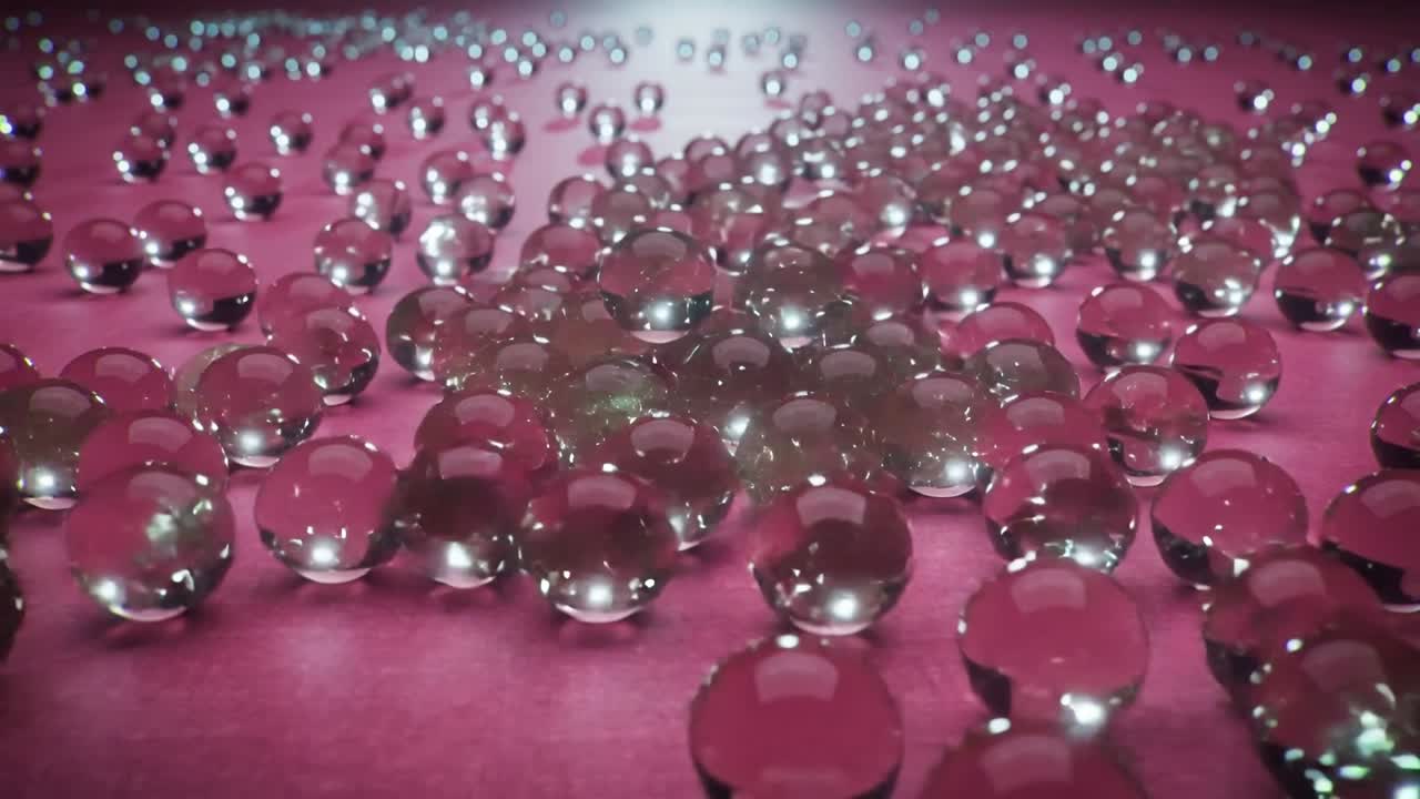 Perline trasparenti che cadono formando un denso grappolo su un tappetino rosa, telecamera che si muove in avanti spostando i riflessi