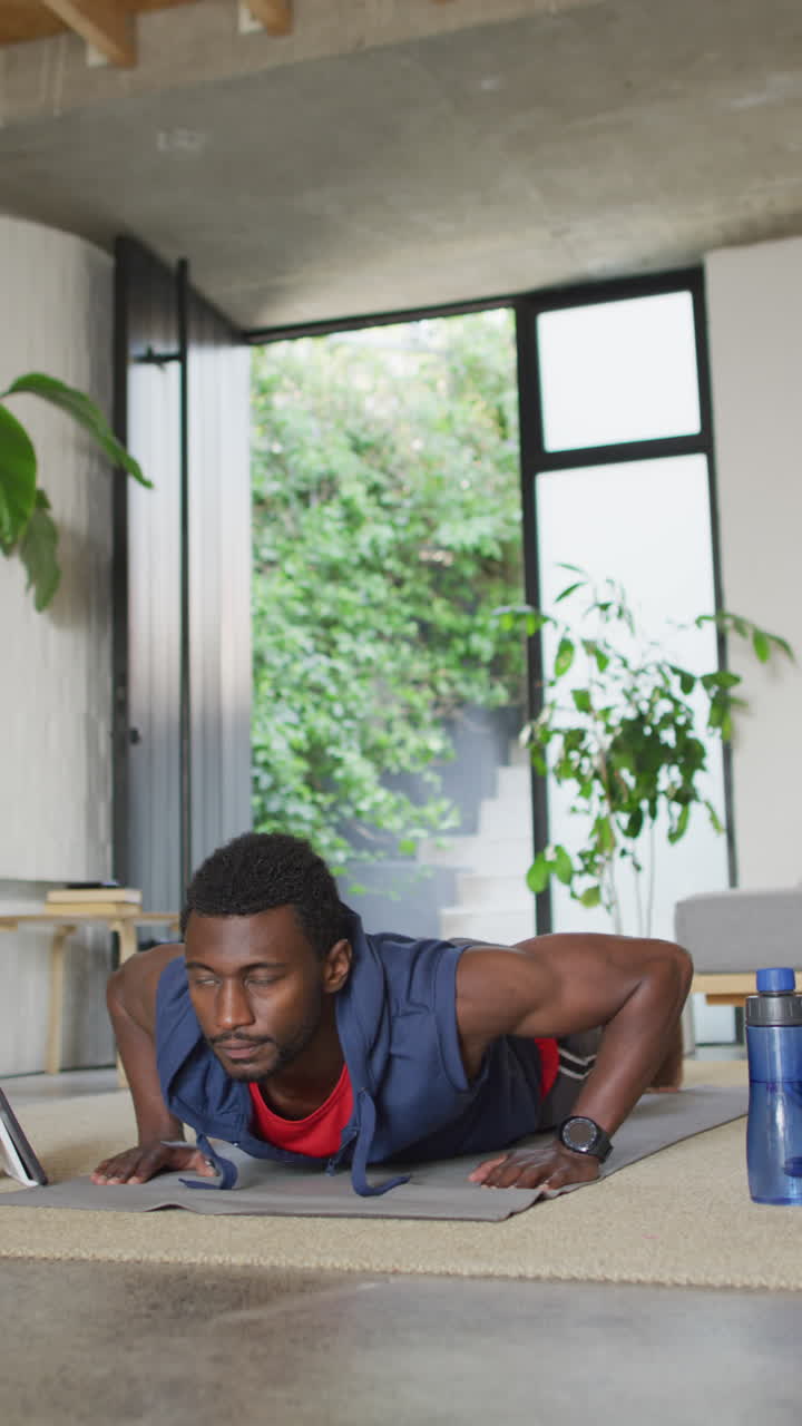 Vertical video of african american man exercising in living room