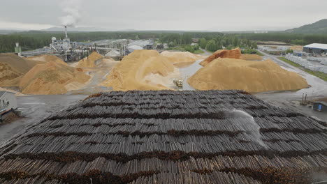 Stacks-Of-Logs-Being-Irrigated-With-Loader-Scooping-Sawdust-From-Stockpile-At-Woodyard-In-Norway