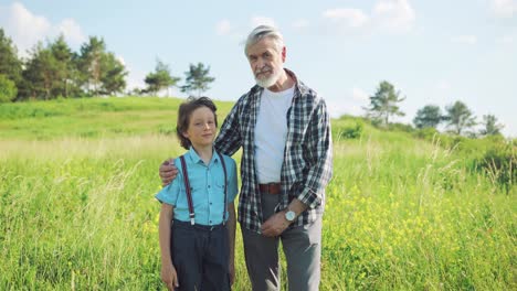 portrait of a senior man hugging to his grandson in the park and looking at camera on a sunny day