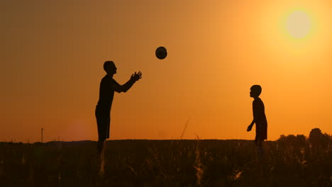 Father-and-son-playing-football-in-the-park-at-sunset-silhouettes-against-the-backdrop-of-a-bright-sun-slow-motion-shooting.