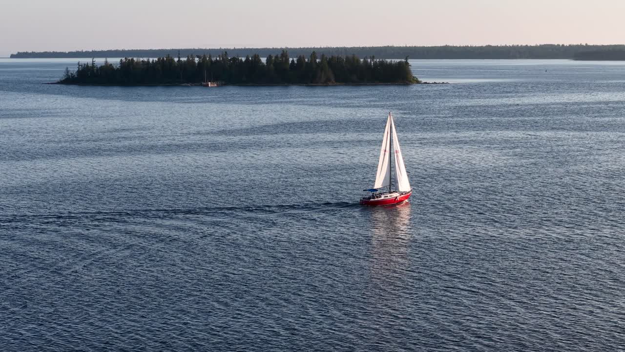 Aerial drone footage of a sailboat gliding across calm blue waters near the Les Cheneaux Islands in Michigan’s Upper Peninsula