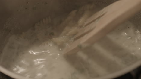 closeup: fusilli pasta cooked in herb sauce, stirred with wood spatula