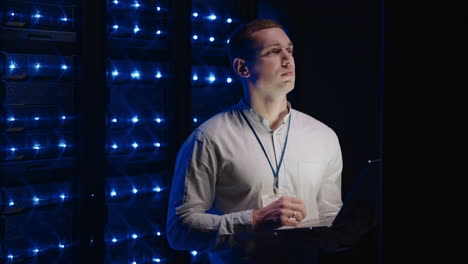 concept of digitalization of information: it specialist in front of server racks with laptop activates data center with a touch gesture. working on a laptop standing before open server rack cabinet