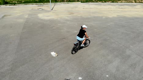 top view bicycle woman riding a bike on round road in abandoned asphalt playground young woman cycling a bike on circle road at summer park. woman riding bicycle on paved road in city square drone view