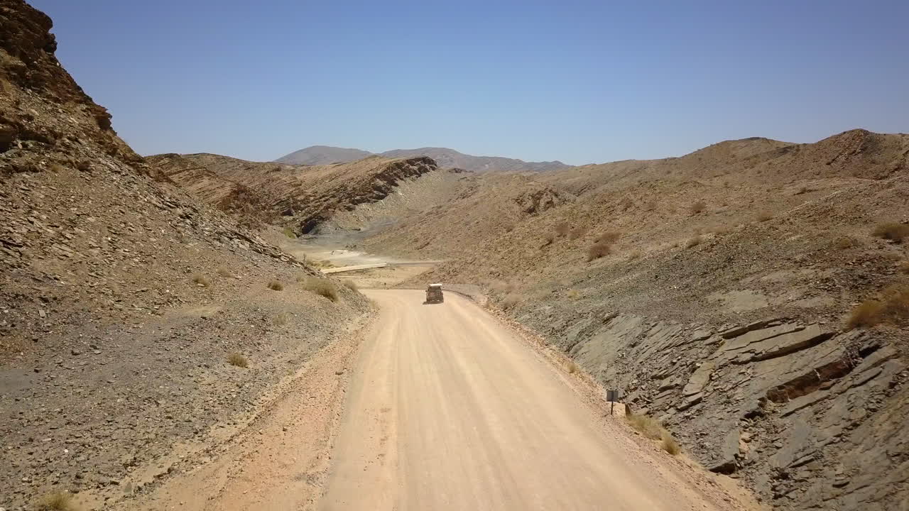 4K footage of a jeep driving along a dusty road in Namibia, captured from a drone following the vehicle. The breathtaking rocky landscape and expansive views the rugged beauty of this African terrain.