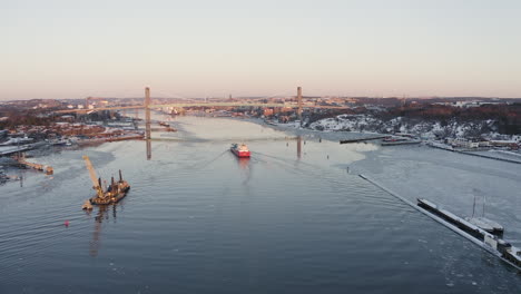 aerial shot of a large red container ship going towards a big bridge and in to the beautiful town gothenburg in sweden