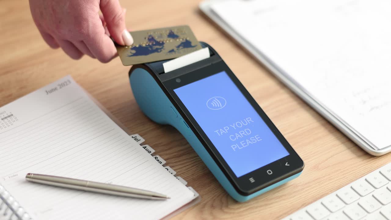 Female holds credit card above wireless payment terminal