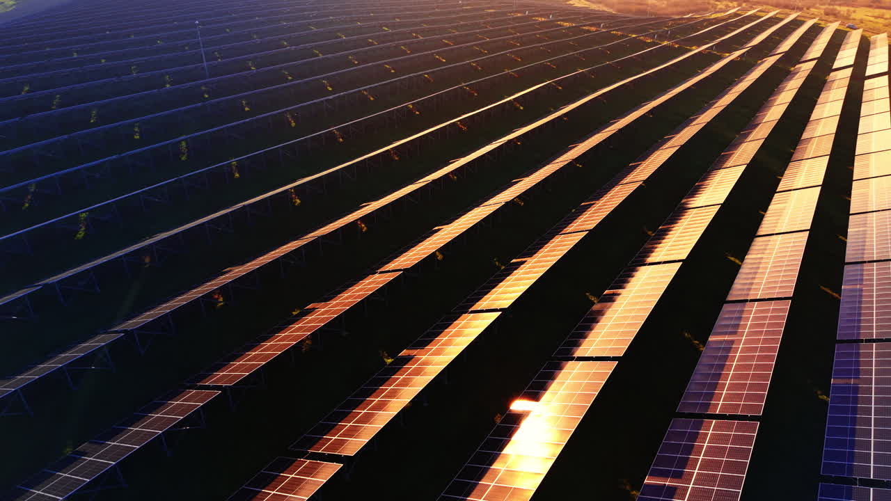 Luftperspektiv af solpaneler under solnedgang. Gyldent lys reflekteres fra glasoverfladen på panelerne med høj kontrast i skyggerne