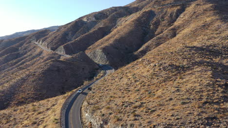 Toma-De-Drones-De-Automóviles-Que-Viajan-Por-Una-Sinuosa-Carretera-De-Montaña-Atravesando-La-Ladera-De-La-Montaña.